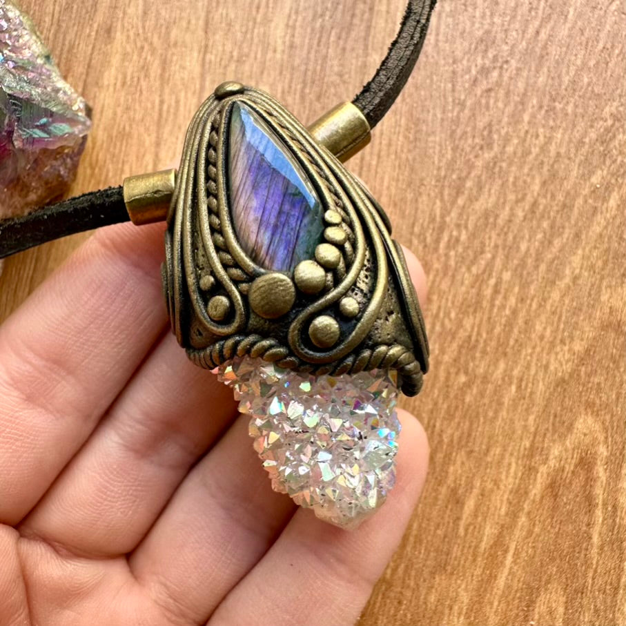 Necklace with purple labradorite and aura quartz crystal held by a hand on a wooden surface