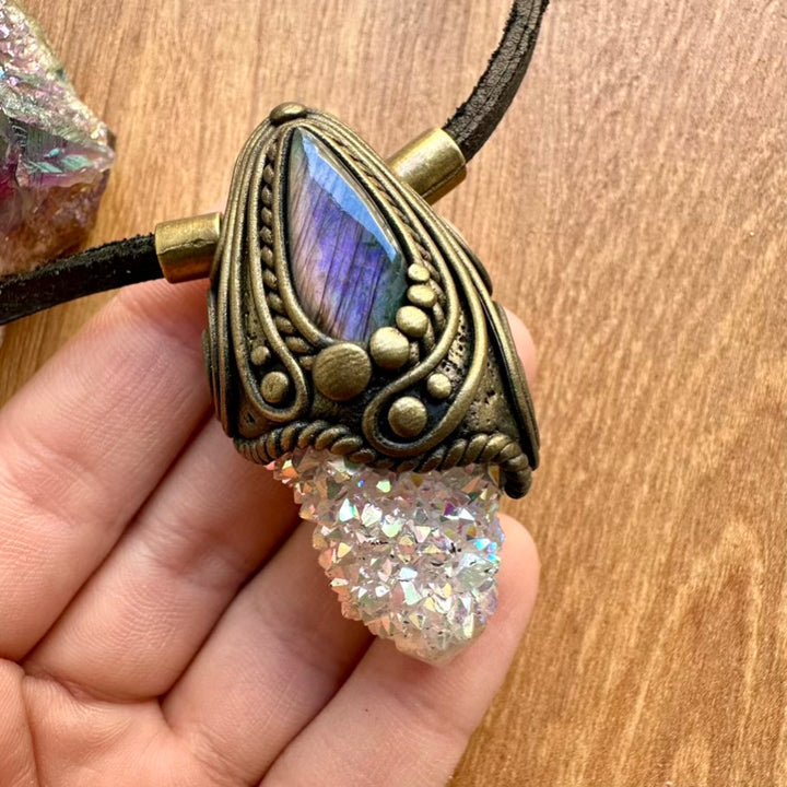 Necklace with purple labradorite and aura quartz crystal held by a hand on a wooden surface