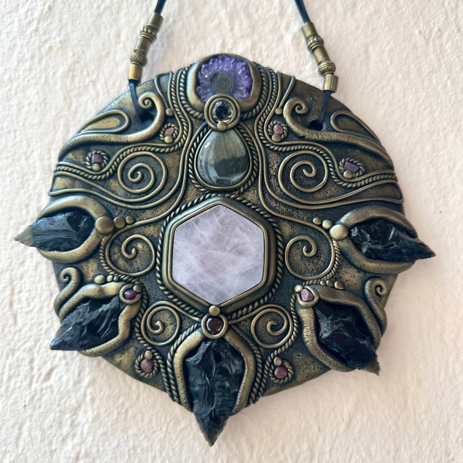 Decorative pendant with intricate designs and gemstones on a beige background