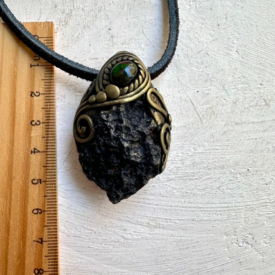 Necklace with a pendant featuring a dark stone and green gemstone, next to a ruler for scale.