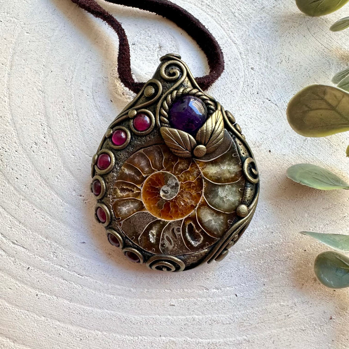 Handmade Ammonite healing crystal necklace featuring Amethyst and Rhodolite Garnet, a one of a kind gemstone pendant combining an ancient natural fossil with rich purple and deep red crystals. Artisan spiritual jewelry crafted with genuine natural materials, inspired by transformation, inner peace, intuition and personal strength.