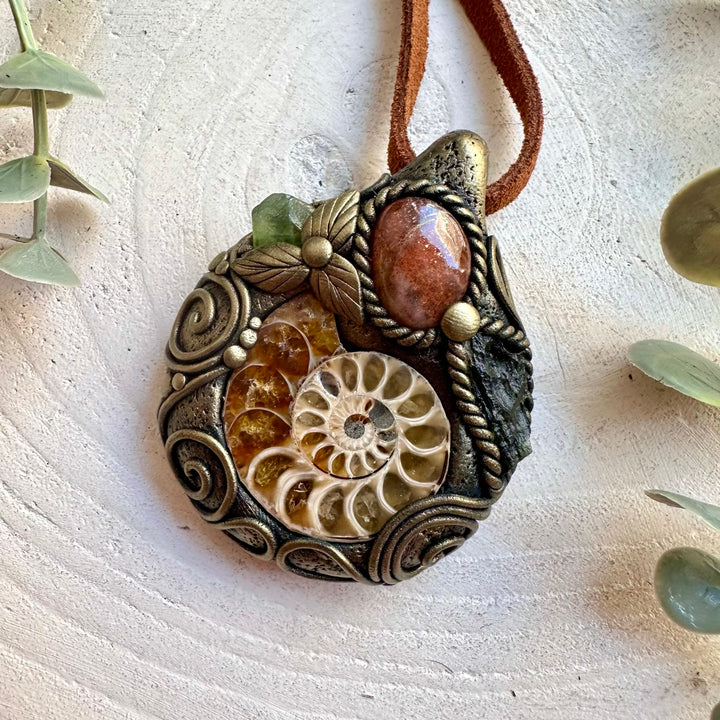 Natural crystal jewelry showcasing an Ammonite fossil with glowing Sunstone and green gemstones.