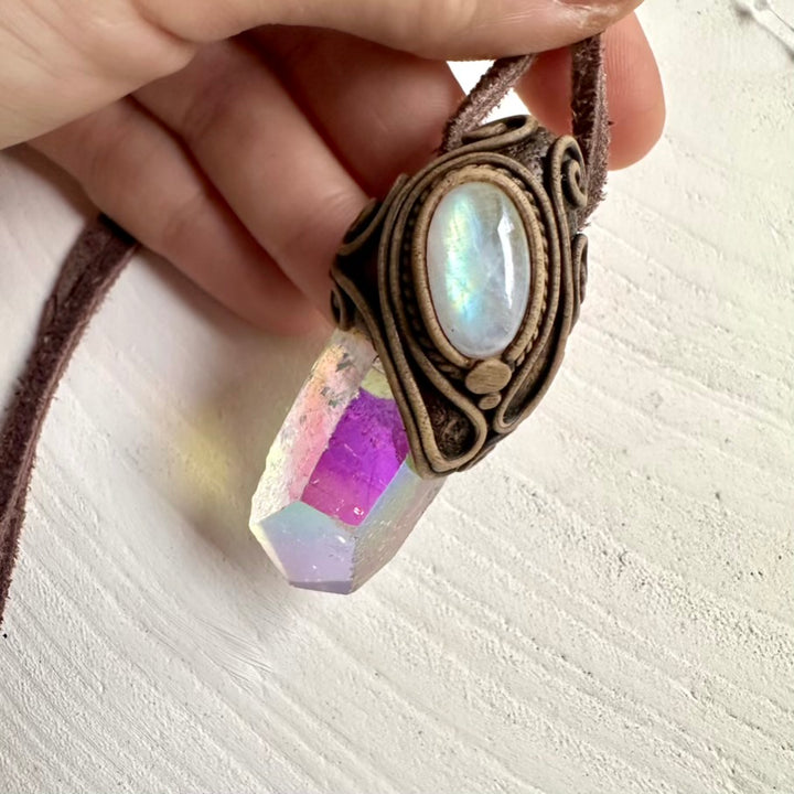 Necklace with angel aura quartz and rainbow moonstone pendant held by a hand on a light background