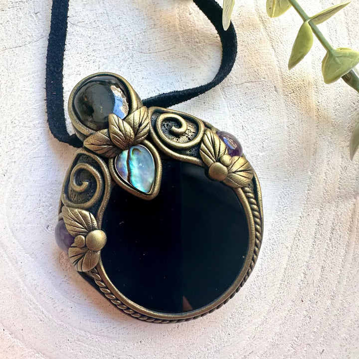 Handmade mystical crystal necklace featuring a Black Obsidian Mirror with Rhodolite Garnet, Abalone Seashell and Amethyst, a unique protection talisman designed for grounding, emotional healing, intuition and inner transformation.