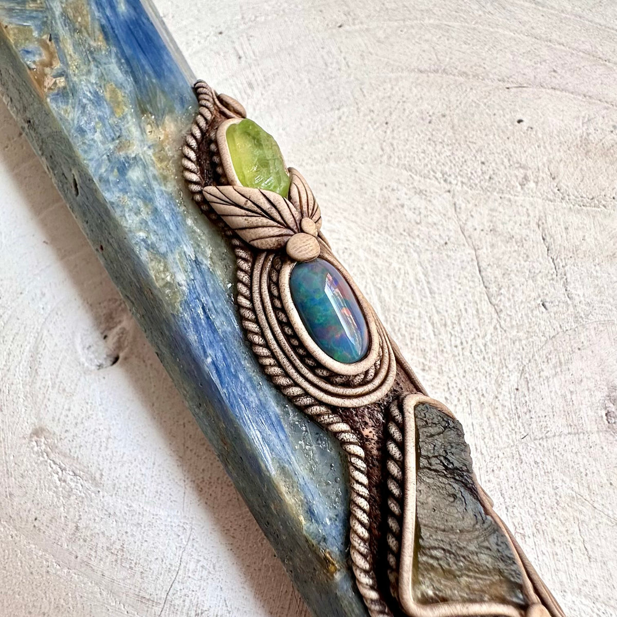 Natural Ammonite and Blue Kyanite form the centerpiece of this unusual crystal wand, accented with Aquamarine, Moldavite and Peridot.