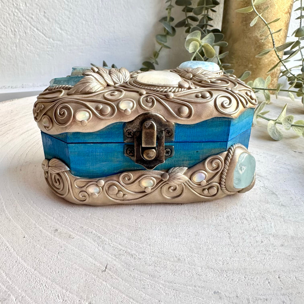 Adorned with a beautiful collection of natural gemstones, this unique decorative box brings together the oceanic colors of Aquamarine and Larimar with the iridescent glow of Aqua Aura Quartz, Rainbow Moonstone and Ethiopian Opal. A magical handmade crystal home decor piece for storing treasured items, creating an altar display, or adding a beautiful spiritual touch to your space.