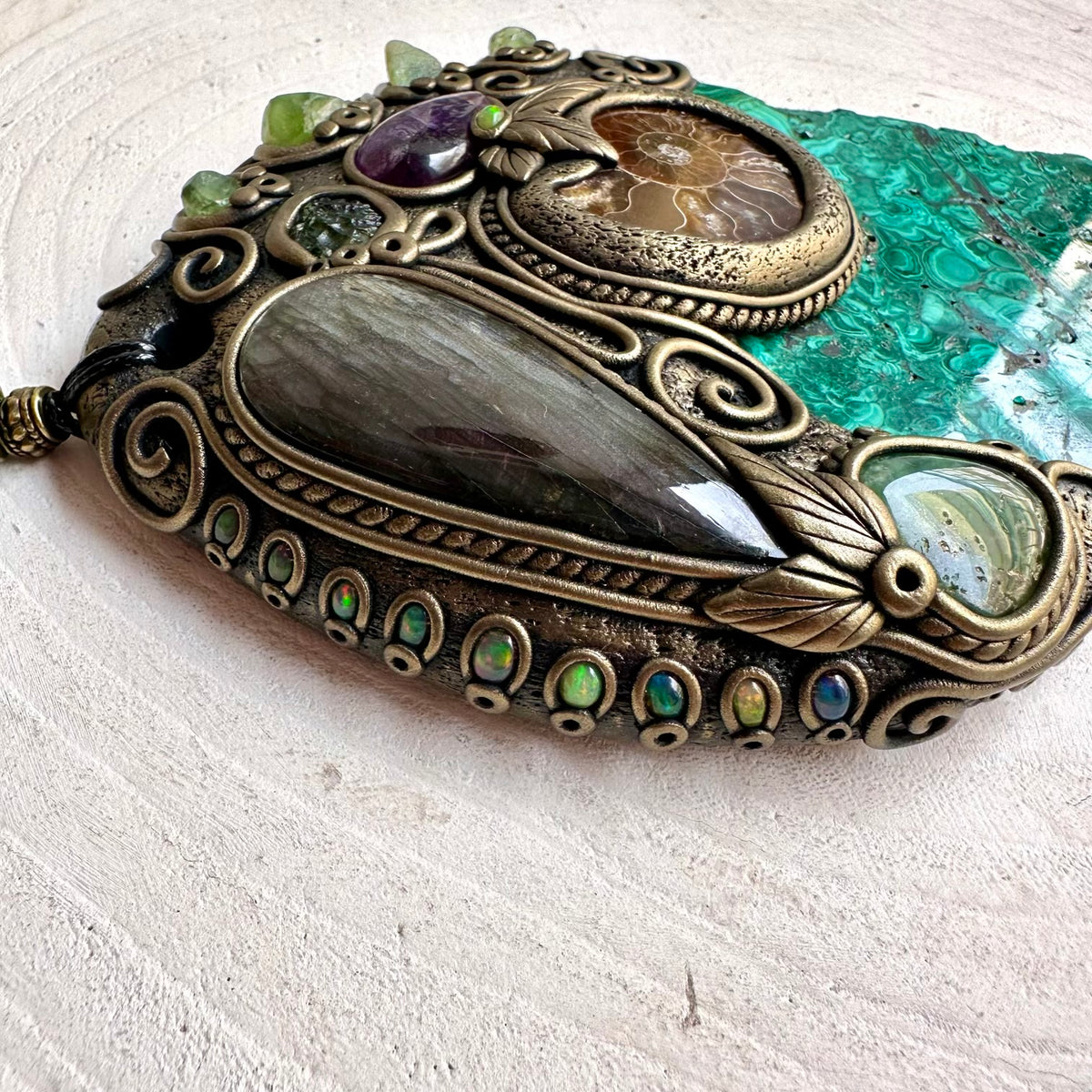Natural Malachite wall hanging and unique handmade crystal home decor, created with Malachite, Labradorite, Ammonite, Peridot, Moldavite, Amethyst, Chrysoprase and Black Ethiopian Opal. This one of a kind spiritual crystal wall art combines vivid natural gemstones with an ancient Ammonite fossil to create a striking piece for a meditation room, altar, sacred space or mystical home interior.