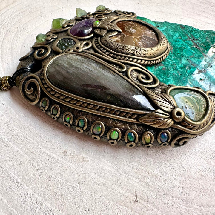 Natural Malachite wall hanging and unique handmade crystal home decor, created with Malachite, Labradorite, Ammonite, Peridot, Moldavite, Amethyst, Chrysoprase and Black Ethiopian Opal. This one of a kind spiritual crystal wall art combines vivid natural gemstones with an ancient Ammonite fossil to create a striking piece for a meditation room, altar, sacred space or mystical home interior.